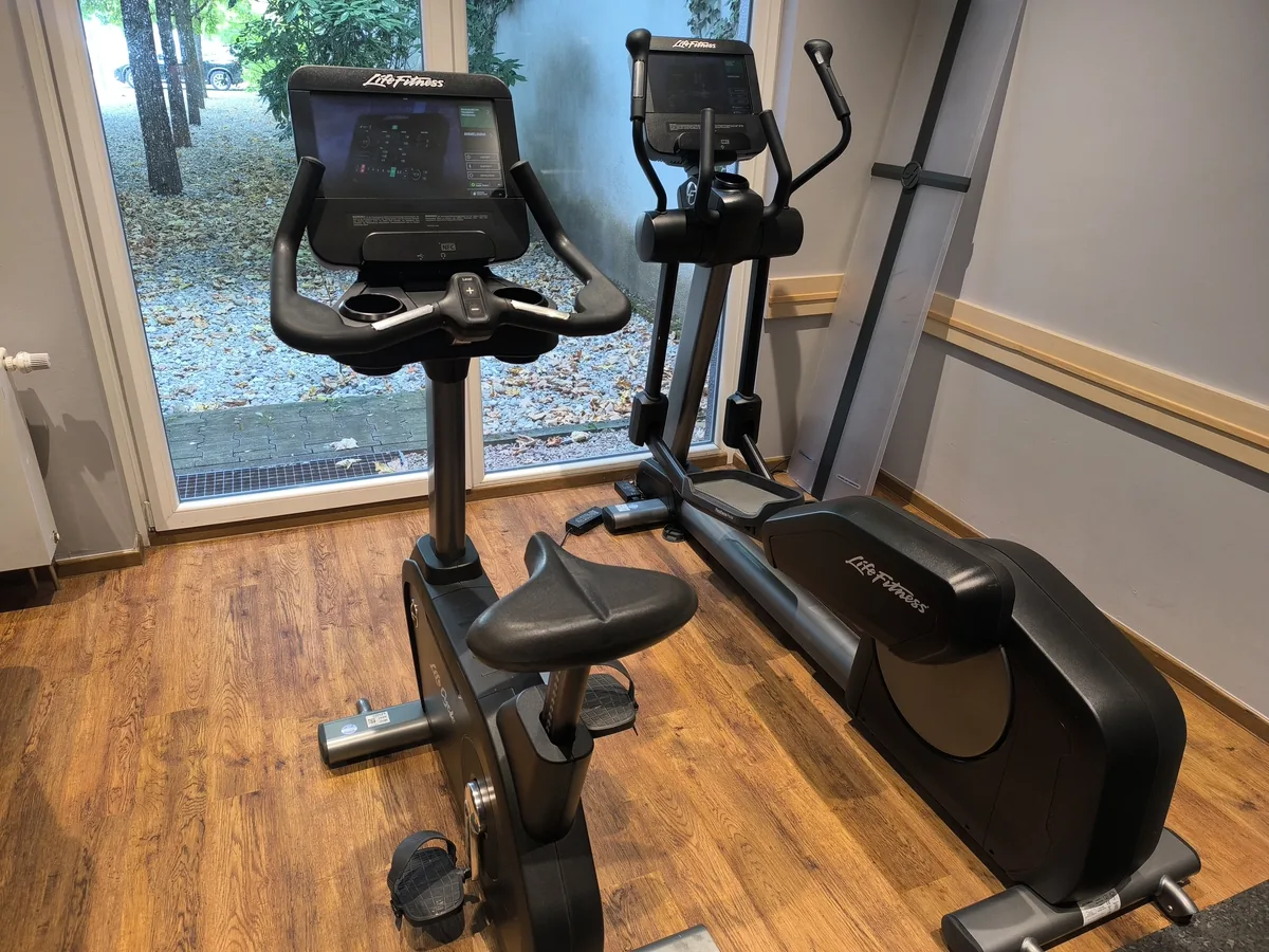 Ergometer und Crosstrainer nebeneinander an einer Fensterfront – TRBS 1201: Prüfungen von Arbeitsmitteln