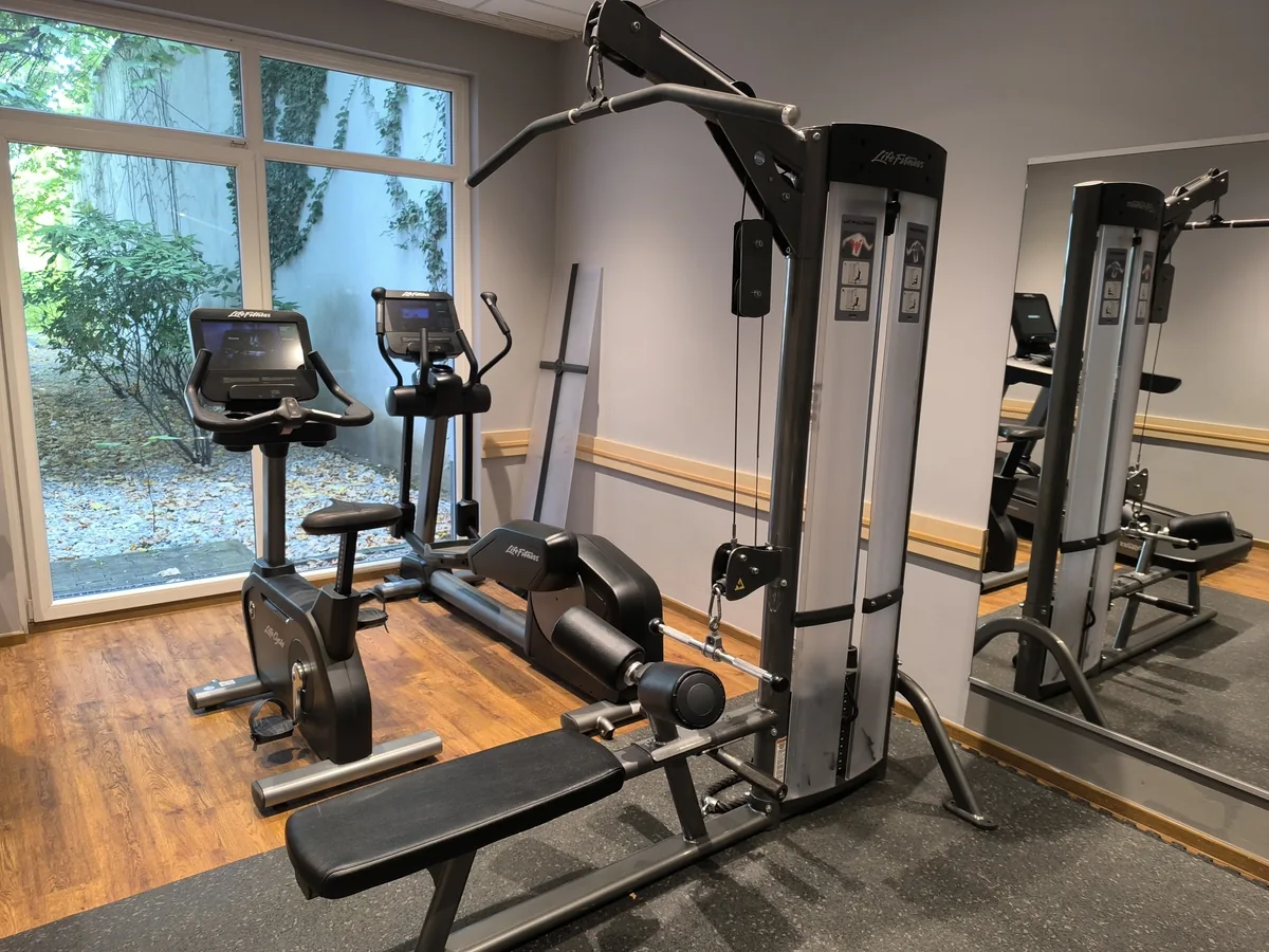 Ergometer und Crosstrainer an der Fensterfront, dahinter eine Kabelzug-Station mit Trainingsbank – Sportanlagen einer Hochschule